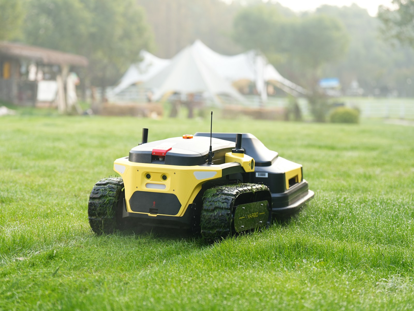 クローラー走行の草刈機が斜面の芝地で作業する様子。【画像生成プロンプト】professional black tracked robotic mower, park lawn, Japanese premium industrial catalog photo, restrained saturation
