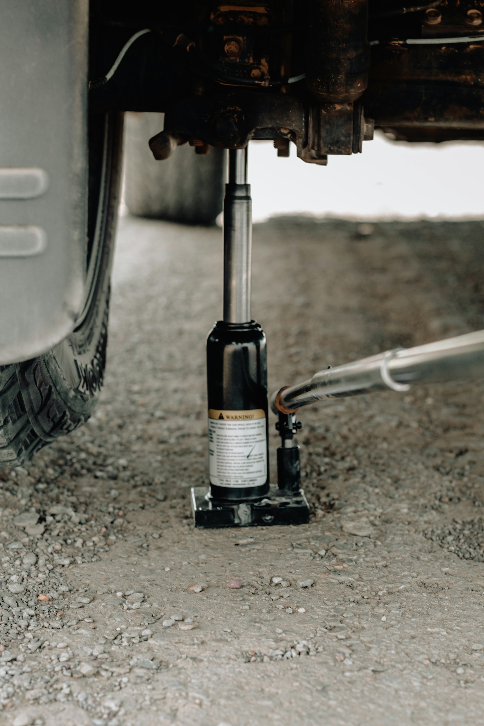 油圧フロアジャッキで車体を持ち上げるメンテナンス。【画像生成プロンプト】blue hydraulic floor jack, concrete floor, crisp daylight, Japanese automotive supplies branding, calm premium look